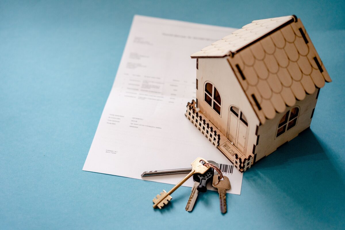 Tiny cardboard house model sitting on a sales receipt along side a set of full size keys representing home ownership