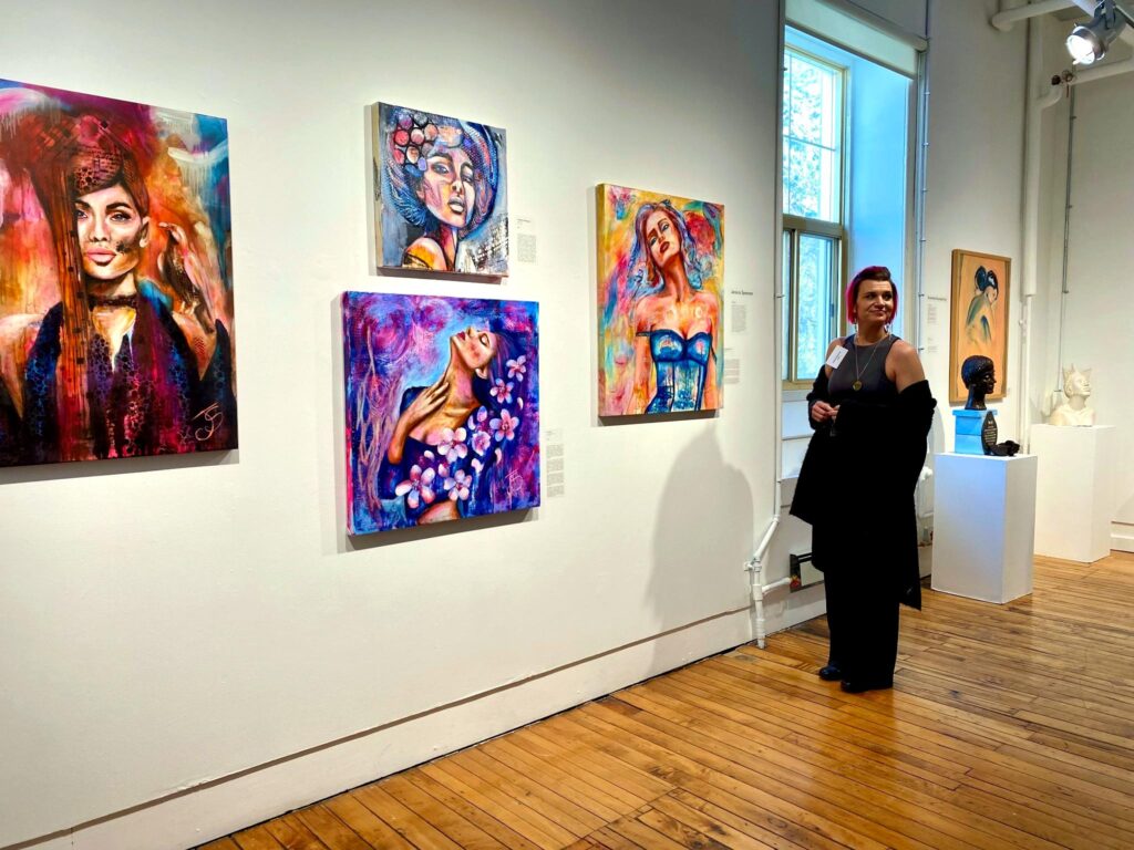 Canadian sovereignty and community resilience expressed through a local artist standing in a gallery beside her paintings, highlighting cultural strength and creativity.