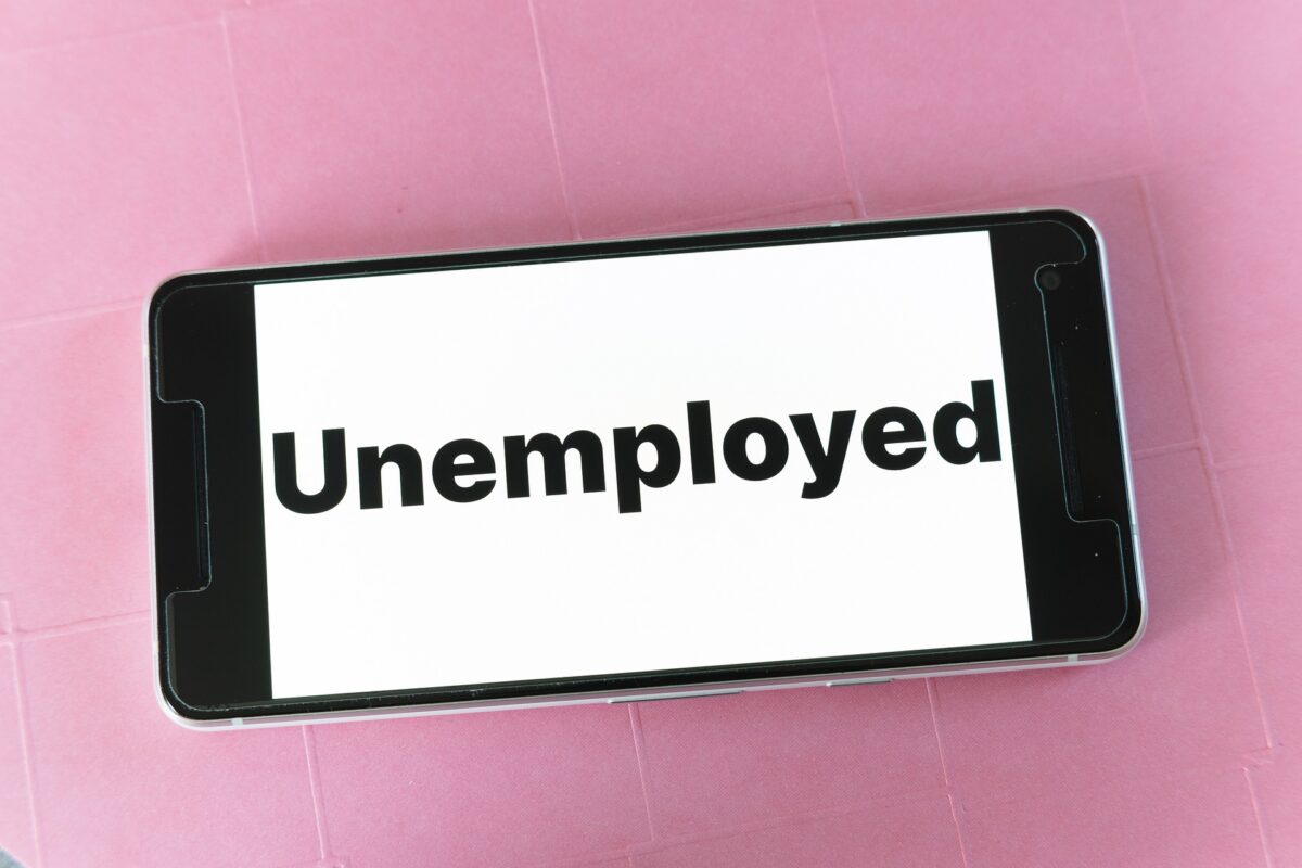 A smartphone screen displaying the word “Unemployed” in bold black letters against a white background, symbolizing joblessness and youth unemployment.